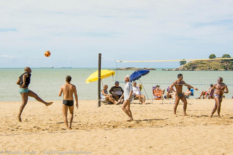 Imagem de meninos no futevolei e umas pessoas sentadas assistindo o jogo na Praia de Cambori.